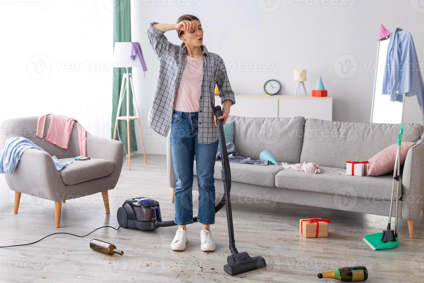 Tired young woman vacuuming her house after party, wiping her forehead, feeling tired of cleaning, free space. Exhausted millennial student getting rid of mess at university dorm room photo