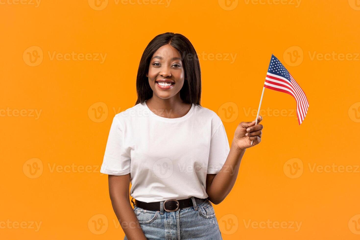 Education abroad, studying in the US, emigration concept. Positive young black woman student holding american flag over orange studio background, panorama with copy space photo