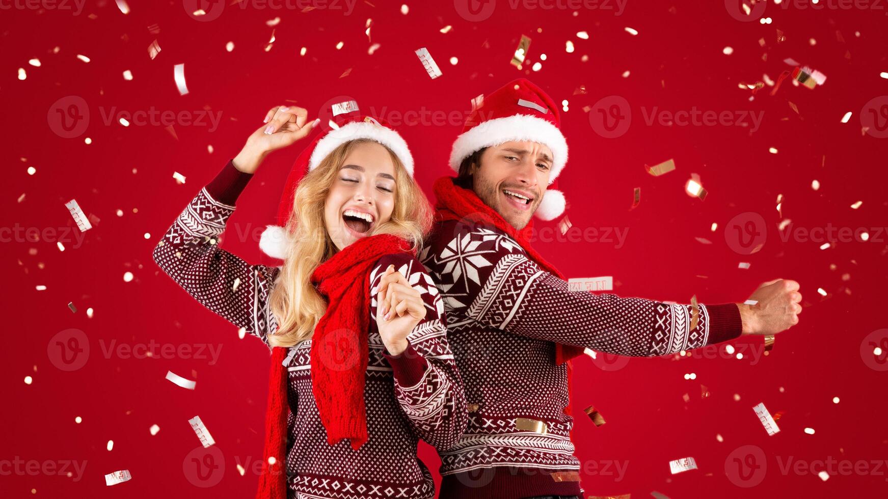 Joyful millennial couple dancing on Christmas or New Year party over red background with falling confetti. Panorama photo