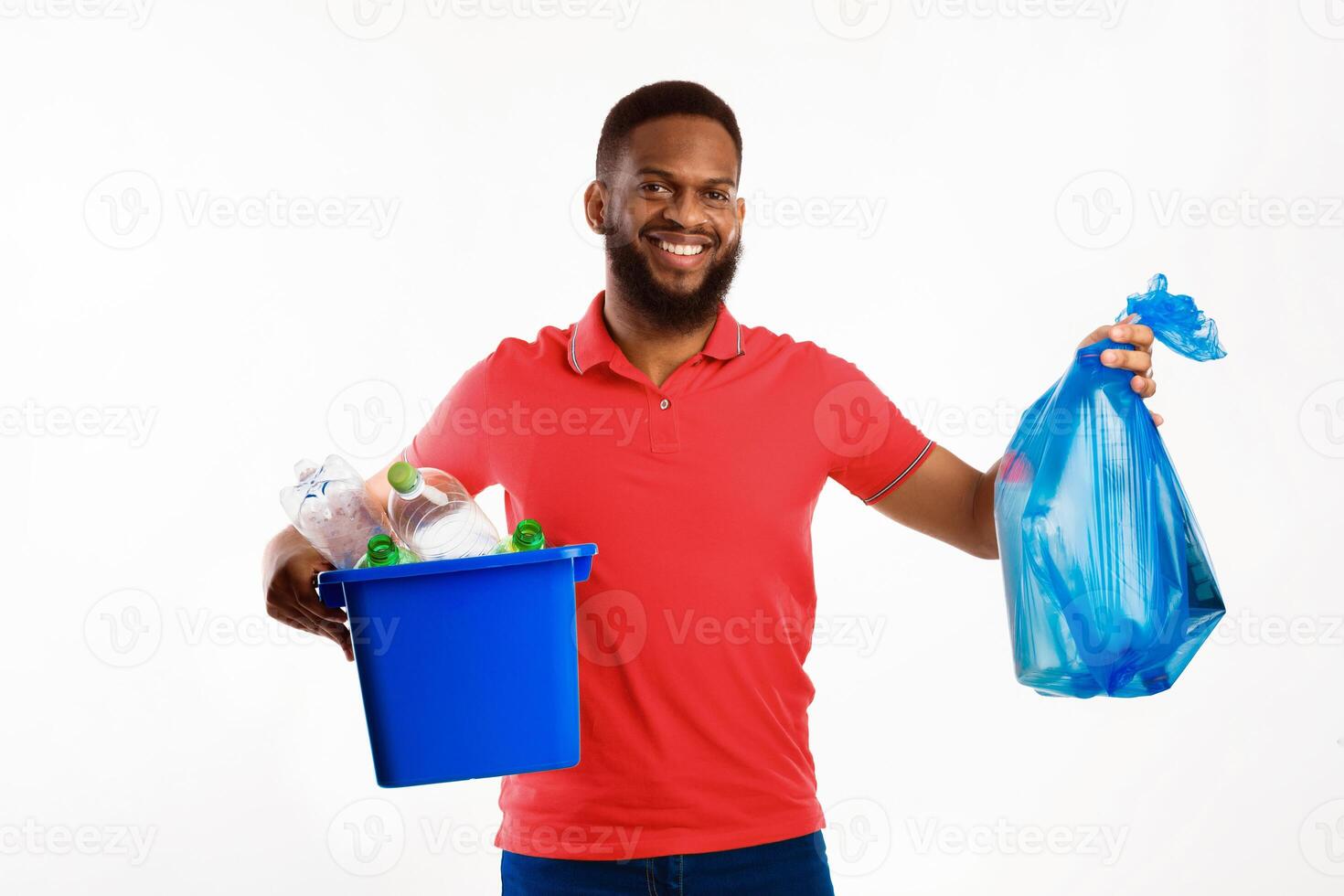 Cheerful Black Man Holding Blue Garbage Bag And Box With Recycle Symbol Plastic Litter Posing Over White Background In Studio. Keep Environment Clean And Sort Your Waste Concept photo