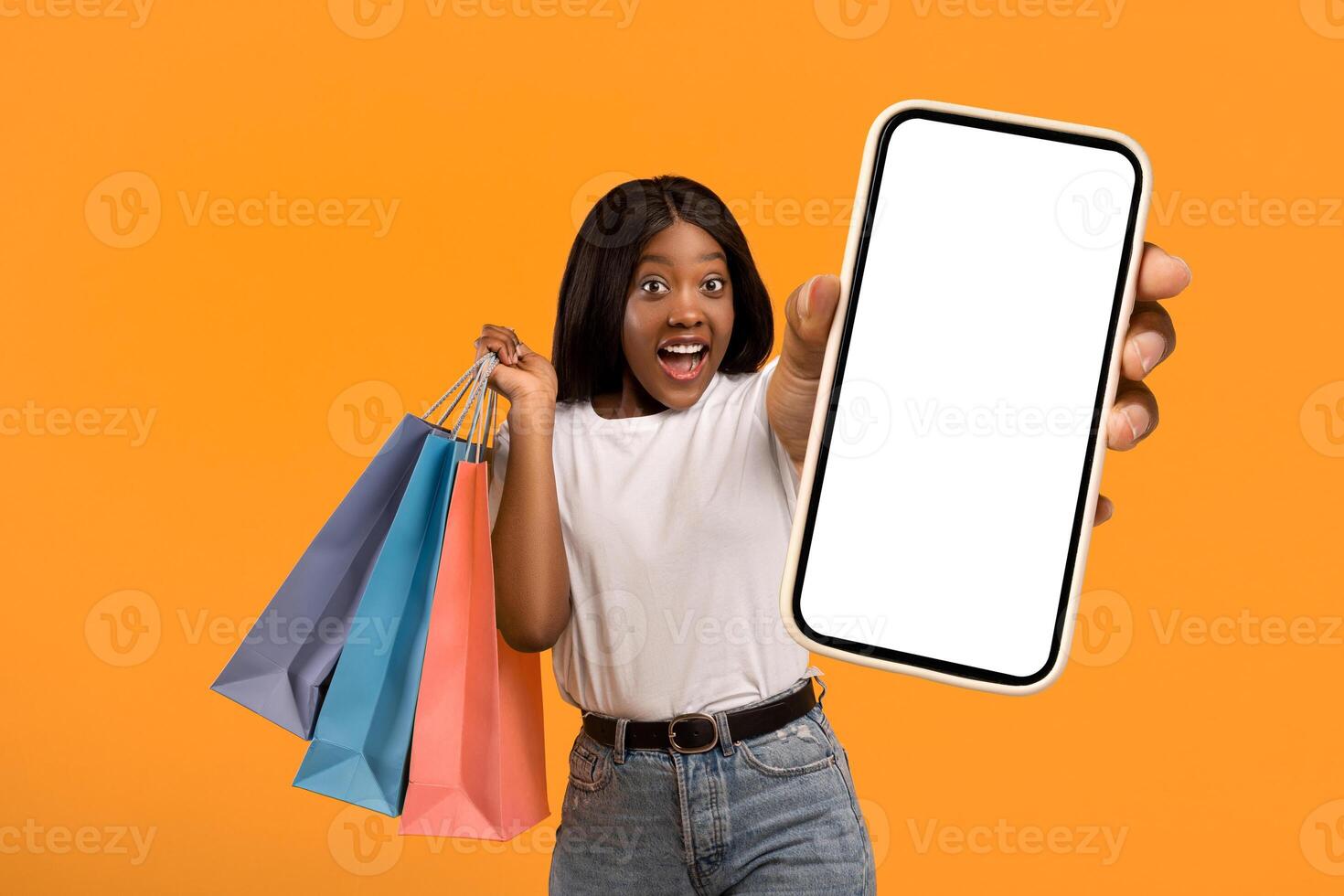 Sales season. Amazed young black lady with shopping bags pointing aside over orange studio background. Shocked african american woman holding purchases, looking at copy space and gesturing photo