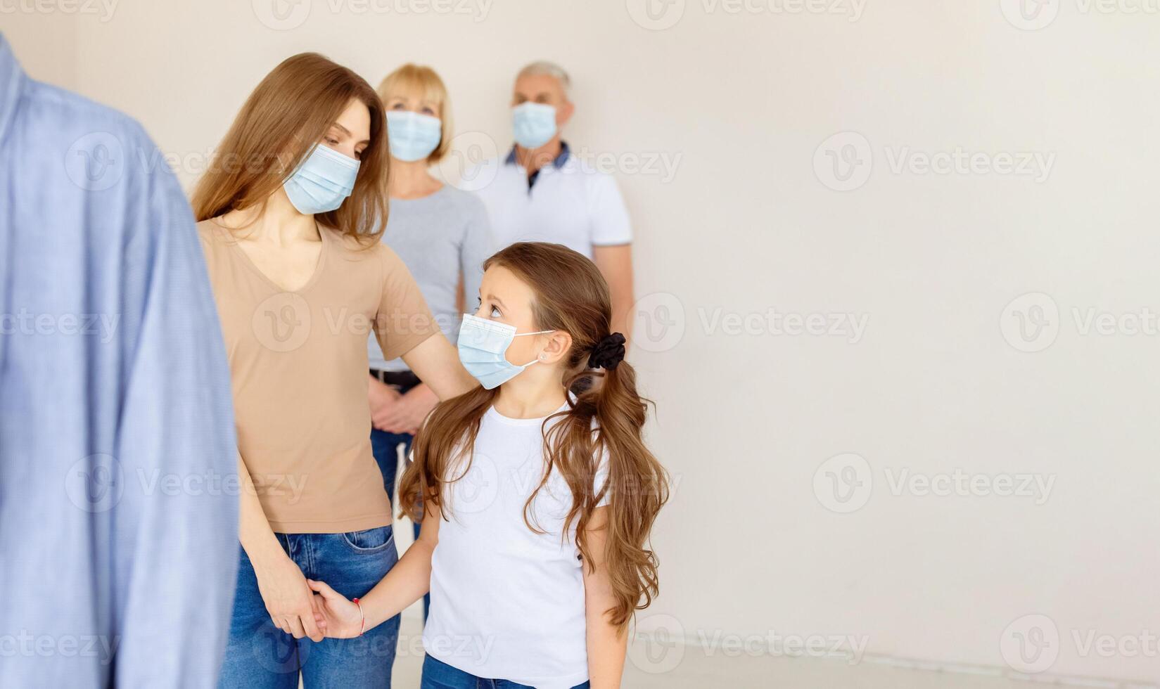 Young mother and her cute daughter in face masks waiting in queue for coronavirus immunization at hospital. Covid-19 vaccination, prevention of global virus spread concept photo