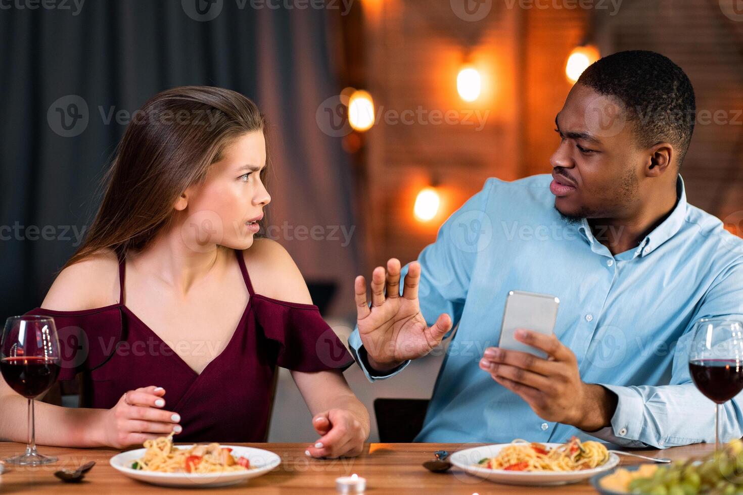 Annoyed Woman Arguing With Black Boyfriend In Restaurant, Blaming Him For Smartphone Addiction, Man Trying To Protect Himself. Young Interracial Couple Having Problems In Relationship, Free Space photo