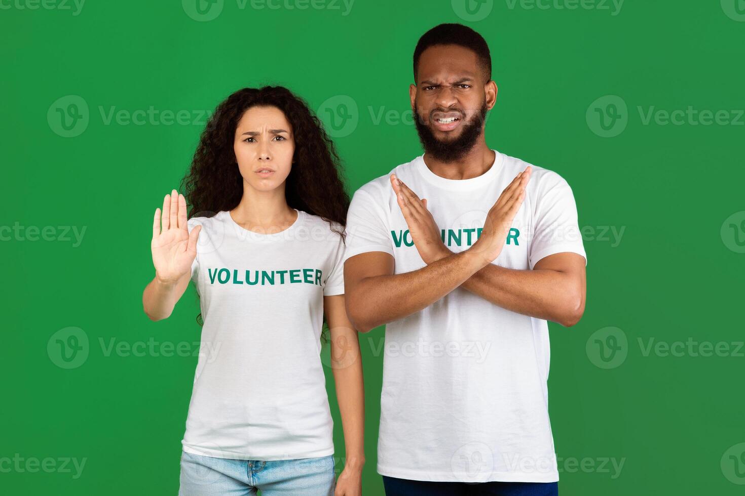 Don't Litter. Two Multicultural Volunteers Gesturing Stop Disapproving And Forbidding Something Standing Over Green Studio Background, Looking At Camera photo