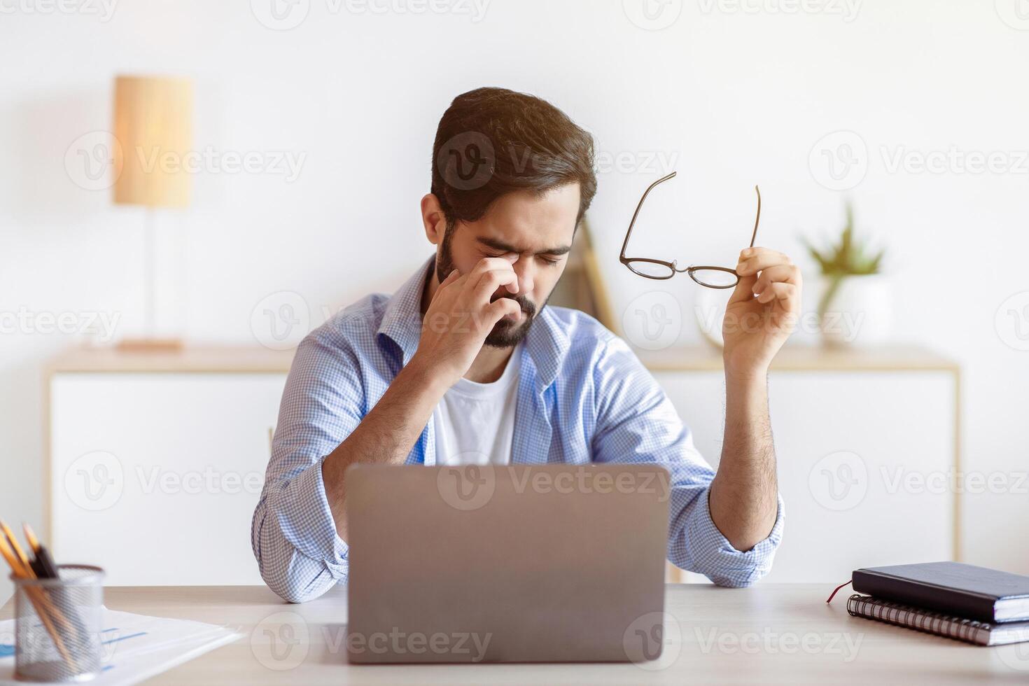 Eye Strain. Tired Arab Freelancer Guy Feeling Exhausted After Working On Laptop, Young Eastern Man Sitting At Desk With Computer In Home Office, Taking Off Glasses And Massaging Nosebridge, Free Space photo