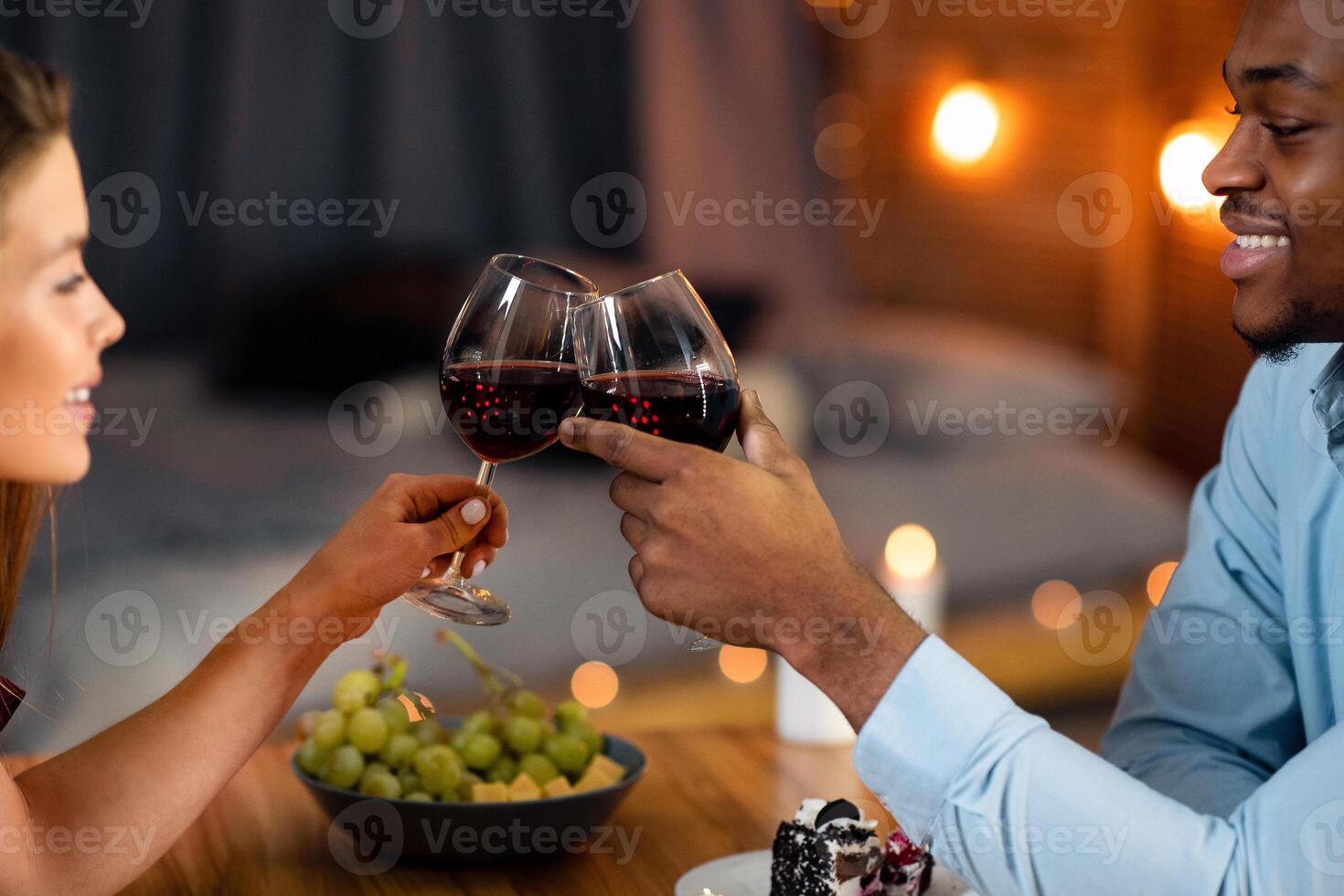 Portrait Of Young Interracial Couple Having Romantic Dinner, Celebrating Valentine's Day Together On A Date In Restaurant, Clinking Glasses With Wine And Eating Dessert, Enjoying Time With Each Other photo
