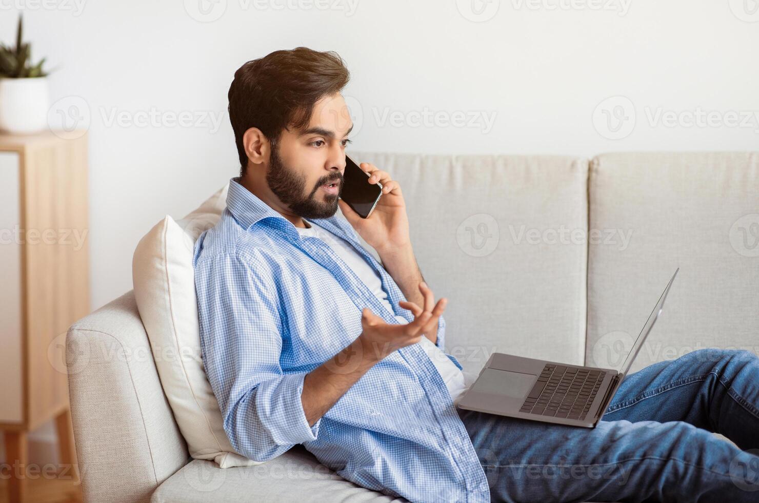 Arab Man Having Problem While Working With Laptop And Cellphone At Home, Eastern Freelancer Guy Suffering Trouble With Internet Connection, Speaking With Customer Service Manager, Sitting On Couch photo