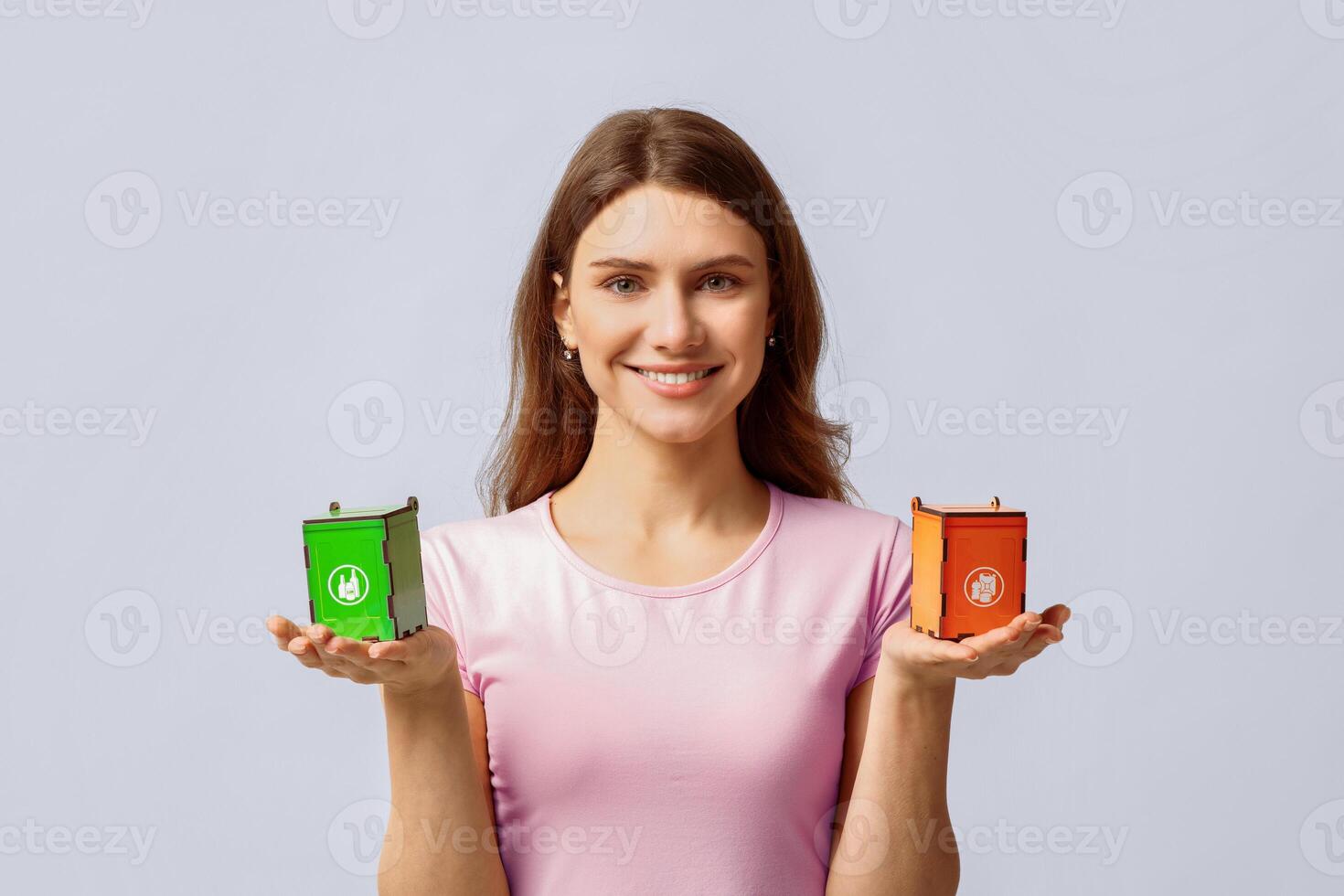 Smiling Millennial Woman Holding Small Toy Recycle Bins For Different Type Of Waste, Standing Over Light Studio Background, Conceptual Image For Garbage Sorting And Trash Recycling, Copy Space photo