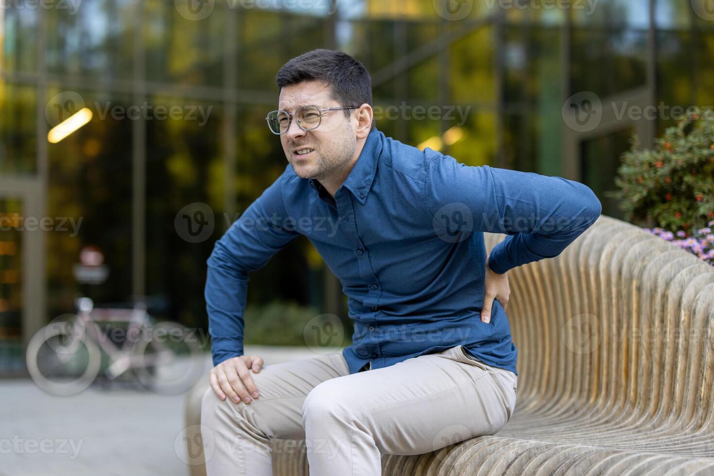 A man sitting on a wooden bench experiencing back pain, showcasing discomfort and distress while sitting. photo