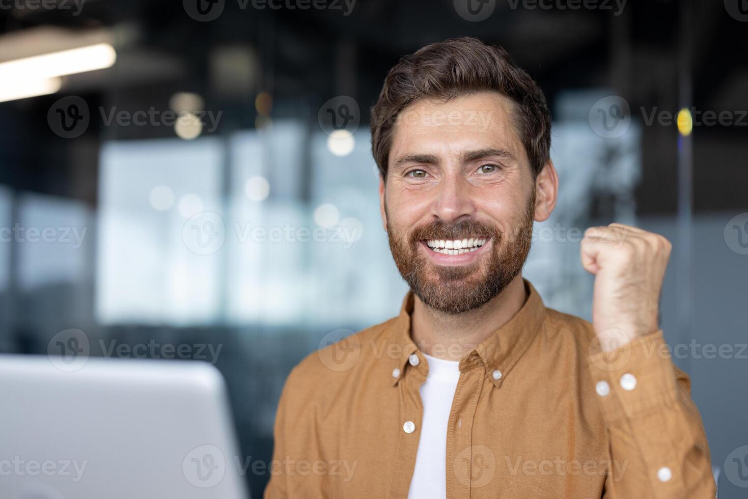 Mature businessman in modern office celebrating success with fist pump and confident smile. Positive attitude, energy, and determination highlighted through engaging expression professional setting. photo