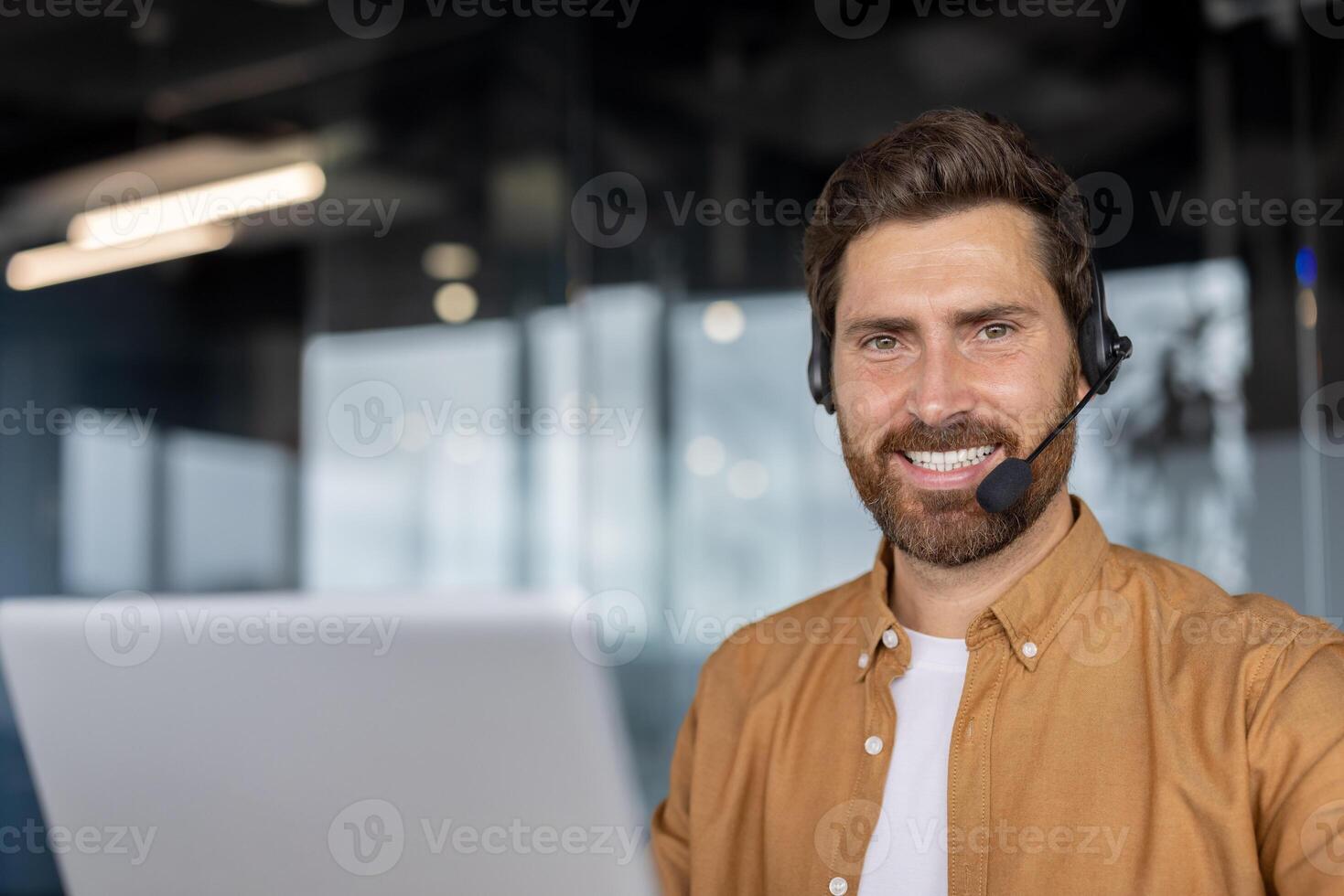 Mature businessman wearing headset working on laptop in modern office. Smiling professional involved in customer service or virtual meeting showcasing connectivity and teamwork. photo