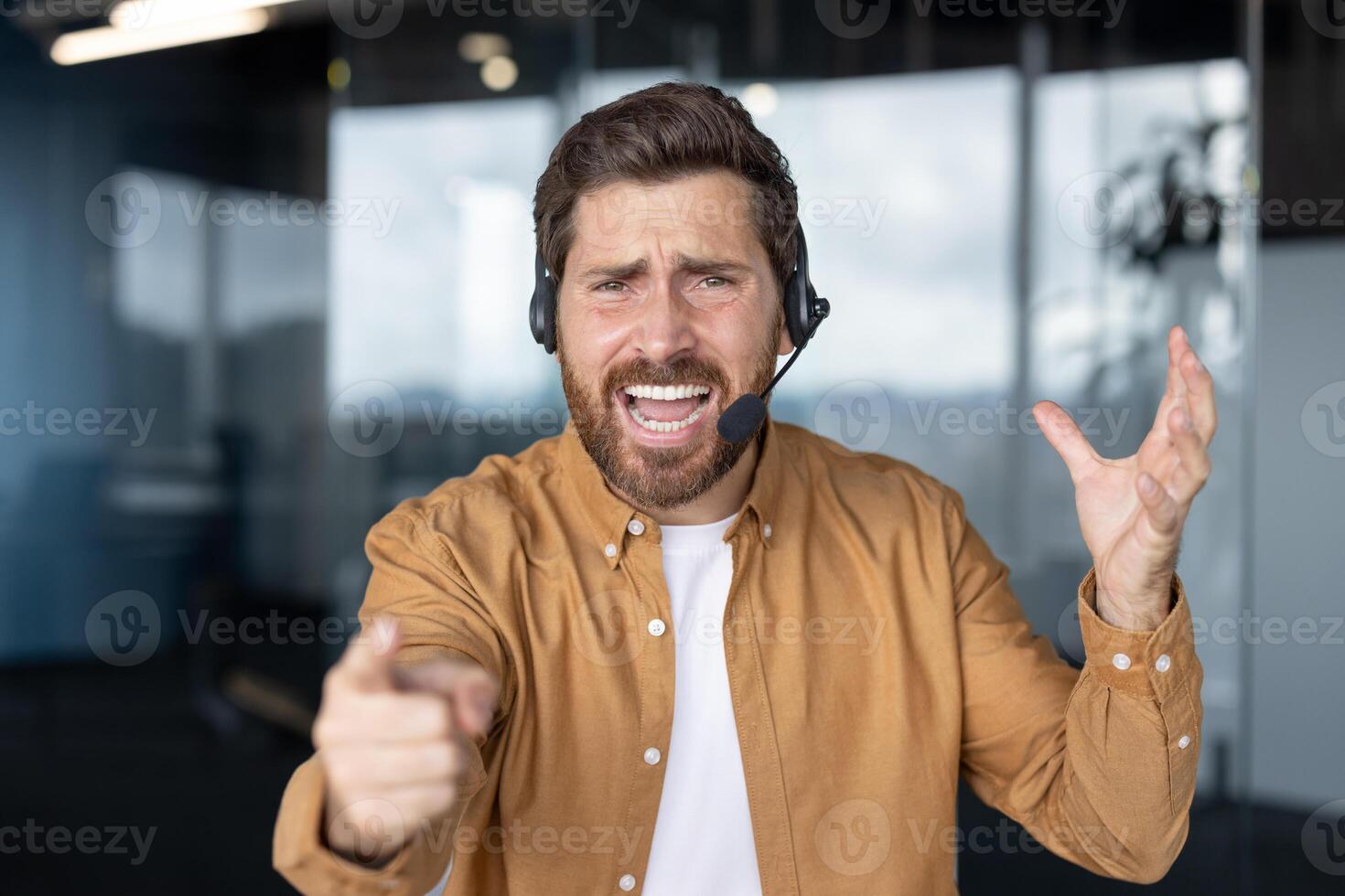 Frustrated customer service representative wearing headset in office expressing dissatisfaction through gestures. Pointing forward with annoyed facial expression suggests stress in workplace. photo