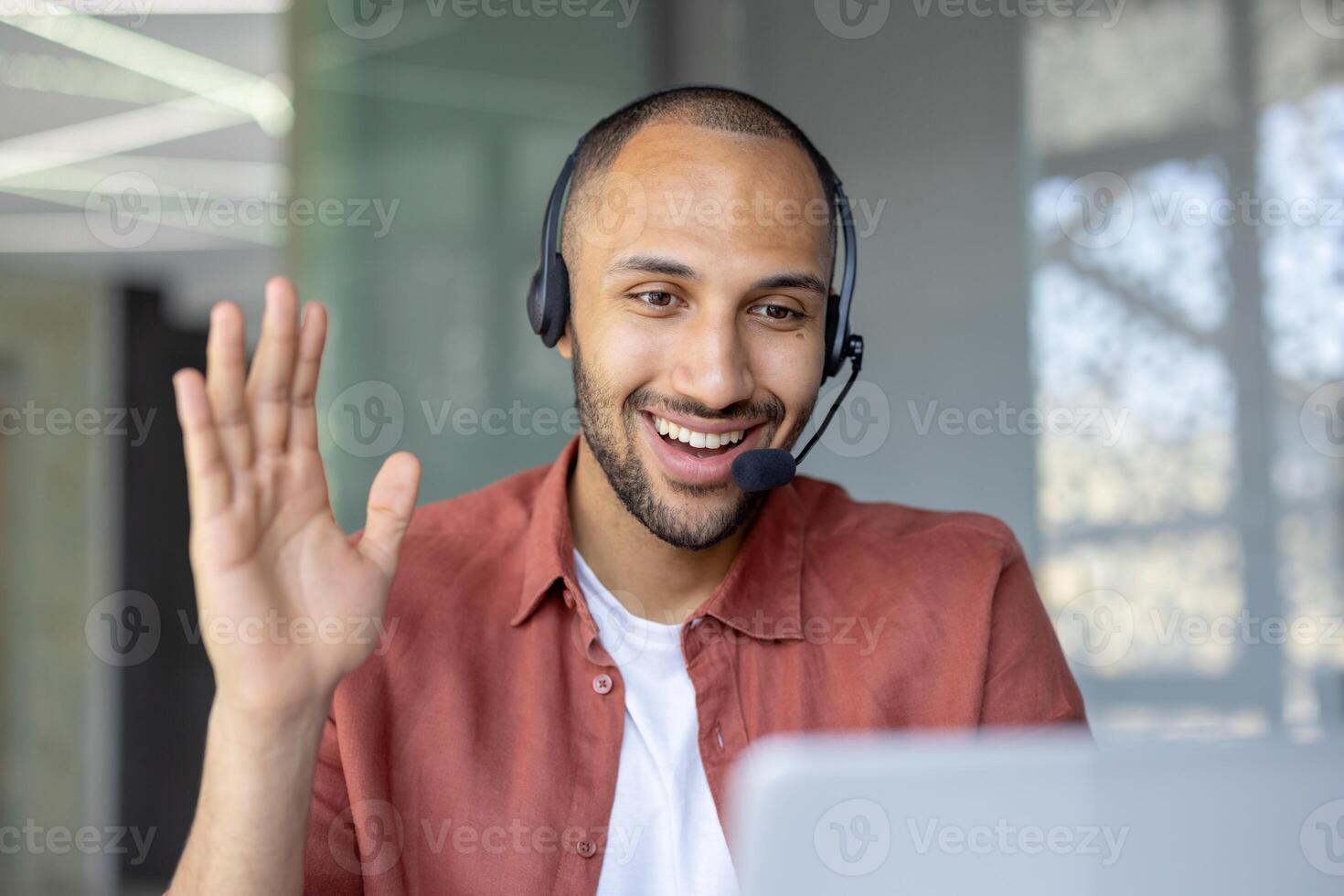 A smiling man wearing a headset waves during a call, engaging in a friendly and professional interaction. photo