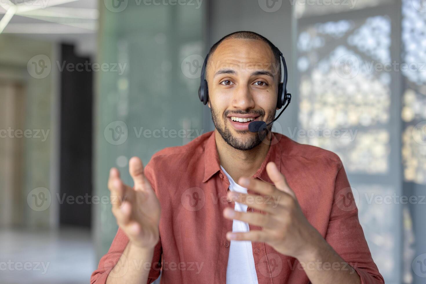 Webcam view, support worker with headset looking into camera, smiling, talking and consulting clients remotely. Man at workplace inside office photo