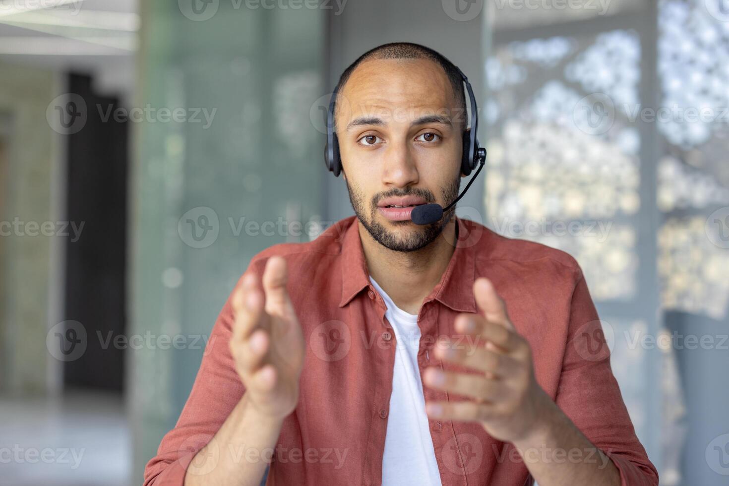 A man wearing a headset gestures while looking directly at the camera. He seems to be in a conference call, or an online meeting. photo