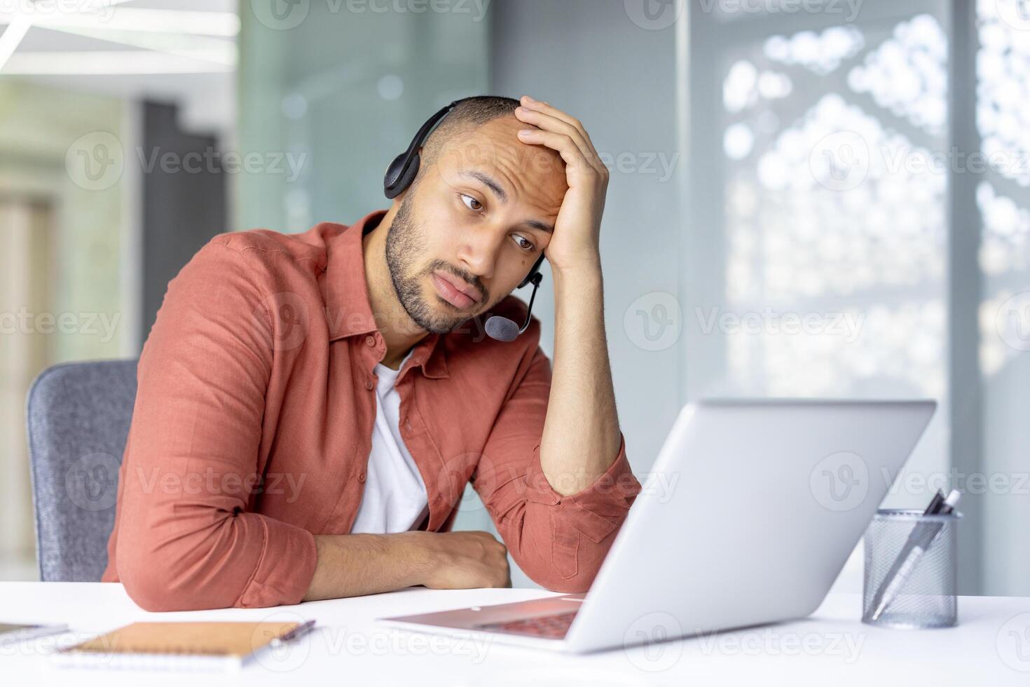 Sad bored man with headset working inside office with laptop, company employee dissatisfied and unhappy at work, consulting clients online. photo