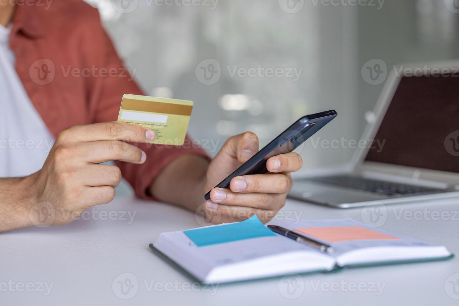 A man is holding a credit card in one hand and a phone in the other, possibly making an online purchase or checking his bank account. photo