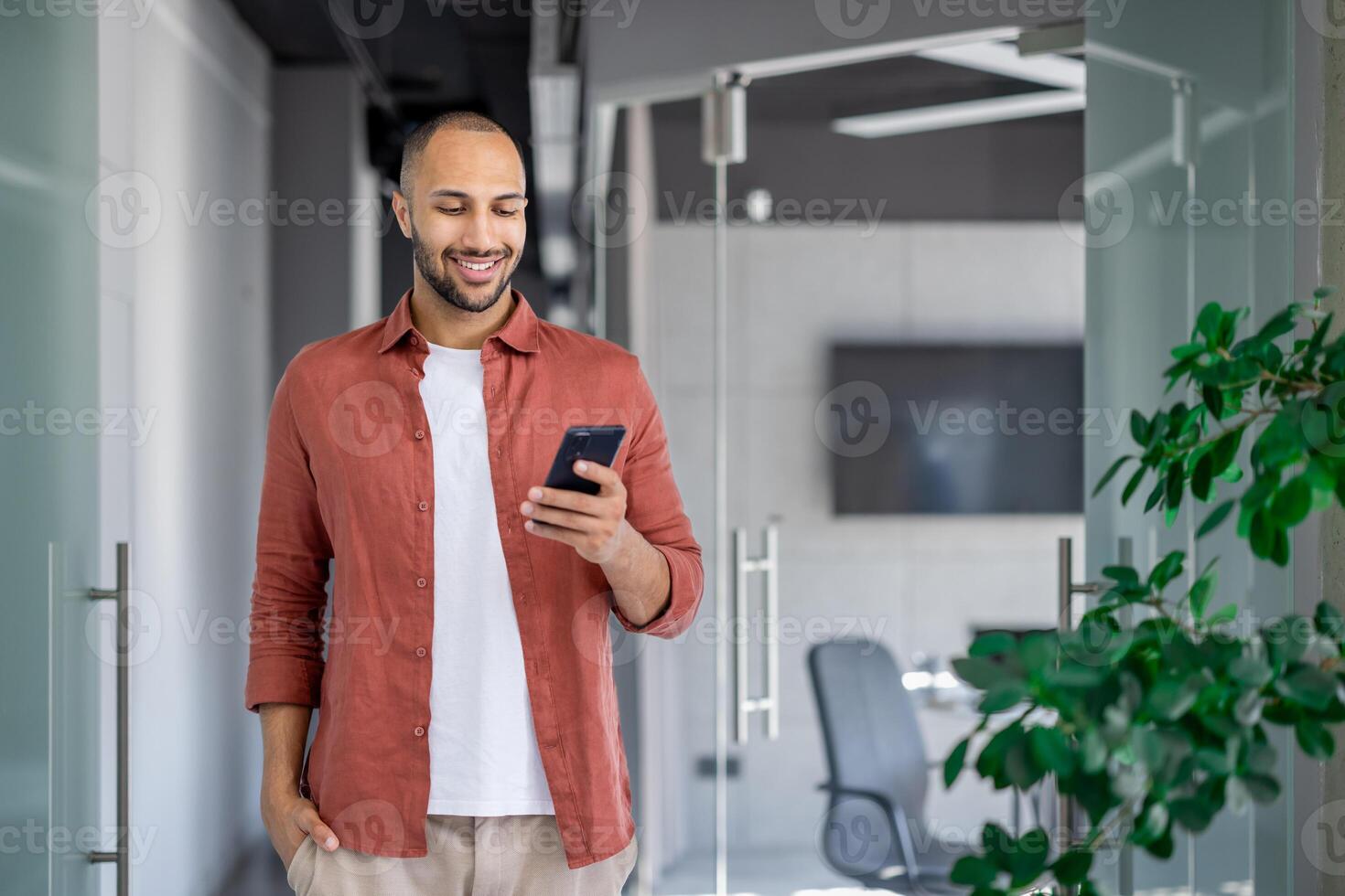 Successful businessman walking through the office with a phone in his hands, the man is typing a text message and smiling, browsing social networks and internet pages at his workplace. photo