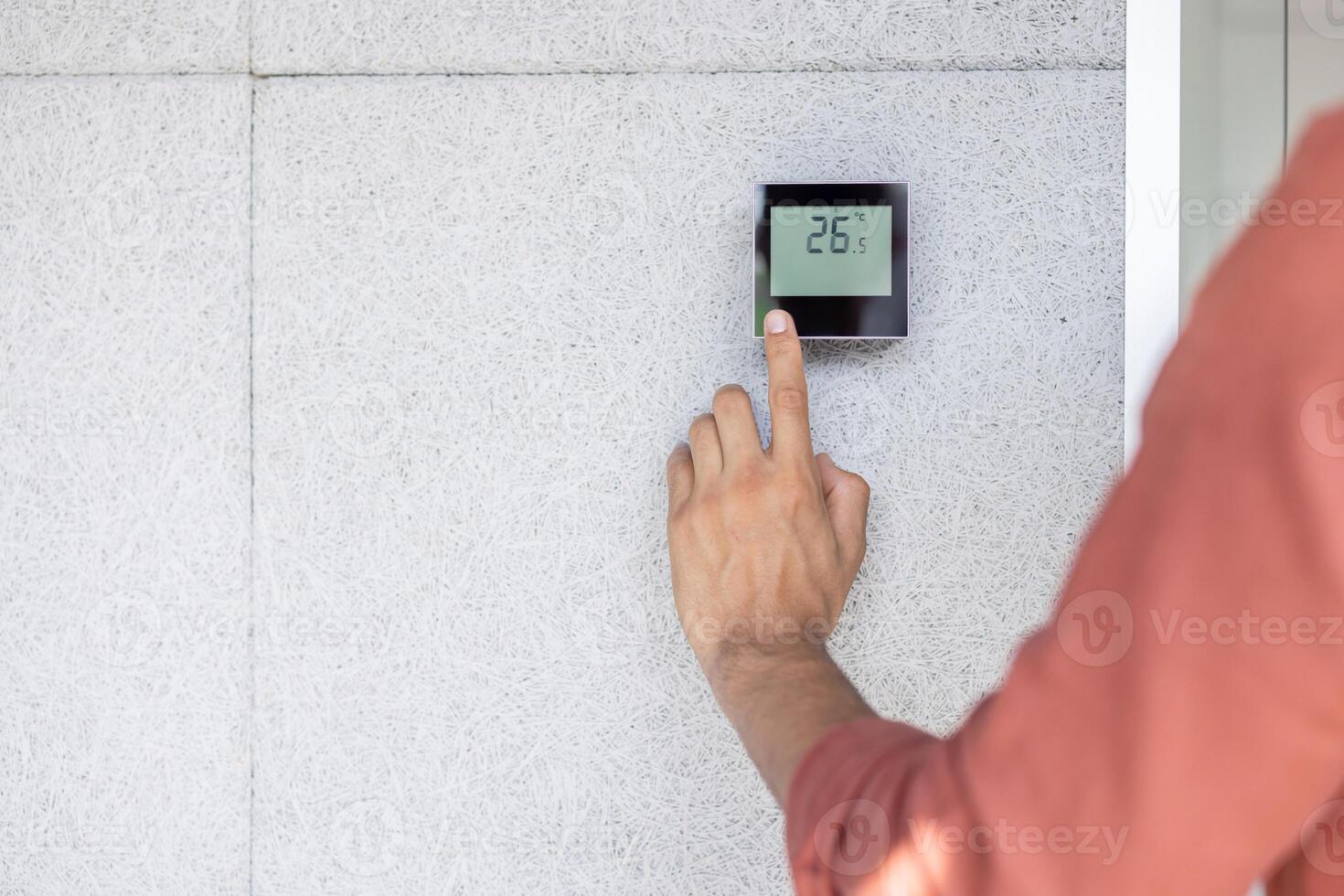 A person adjusts the temperature on a smart thermostat mounted on a textured wall photo