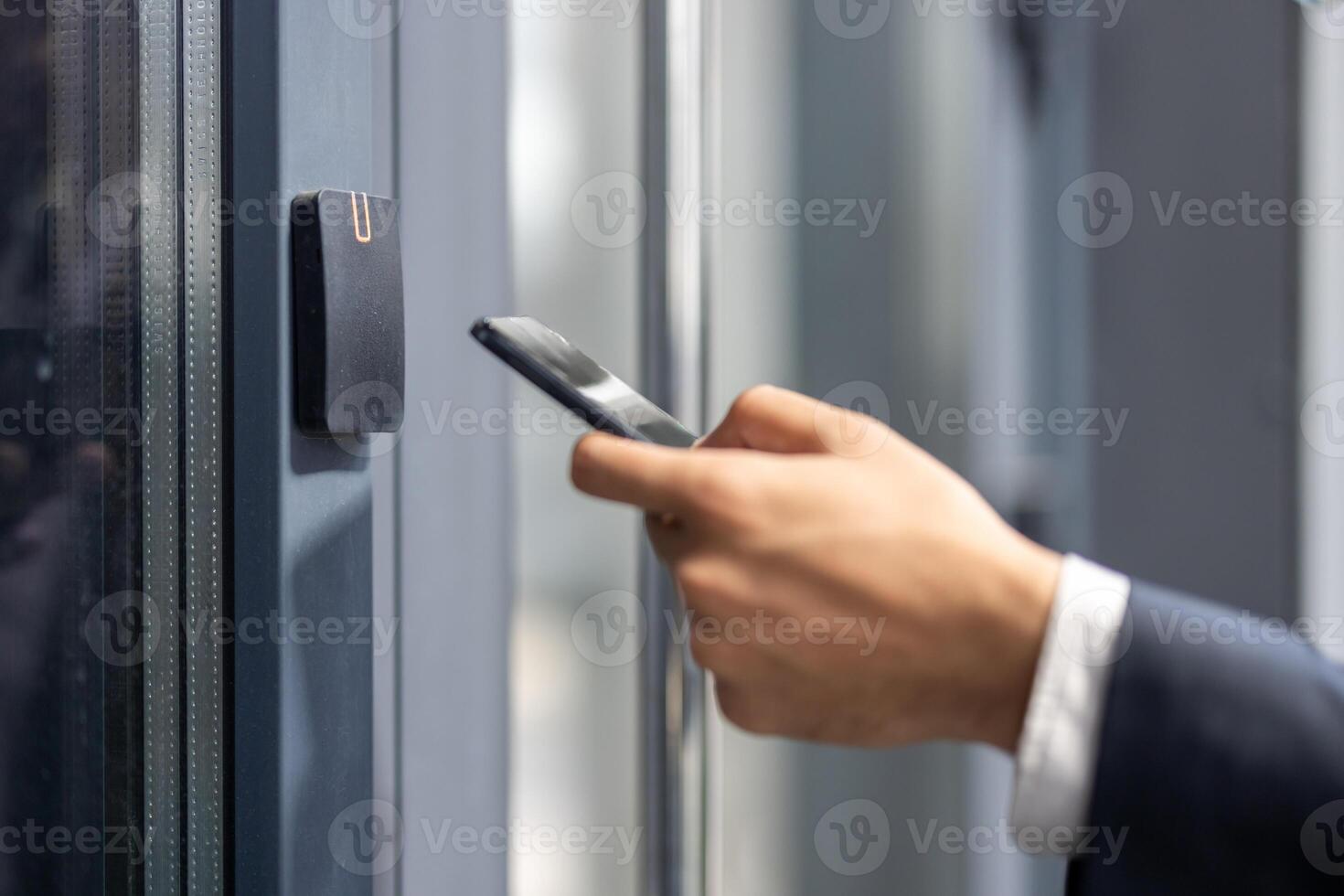 A person in a suit uses a smartphone near a door access system, possibly for security or entry. photo