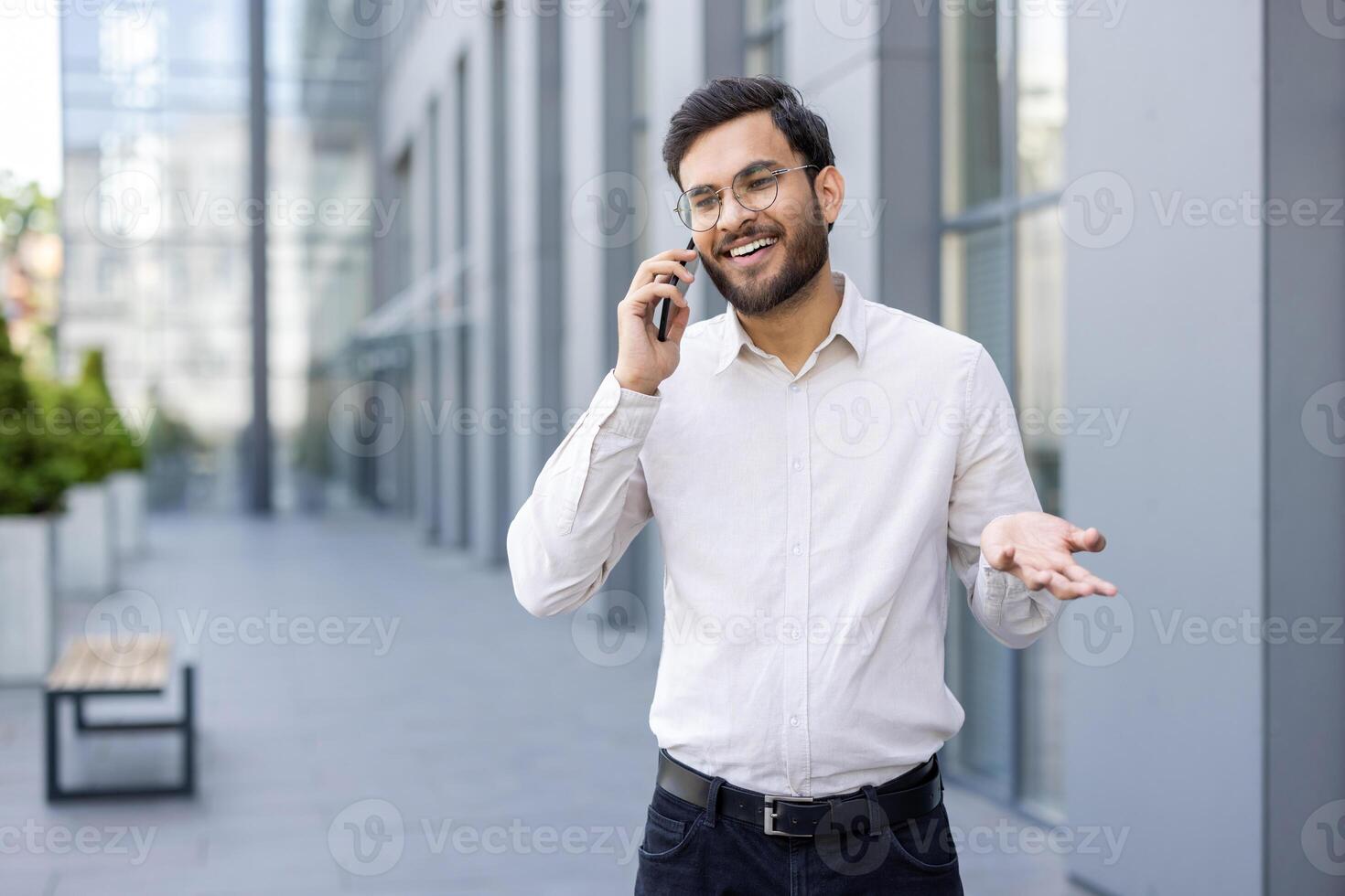 A smiling businessman talks on his phone in front of a modern building. He gestures with his hand while discussing something. photo
