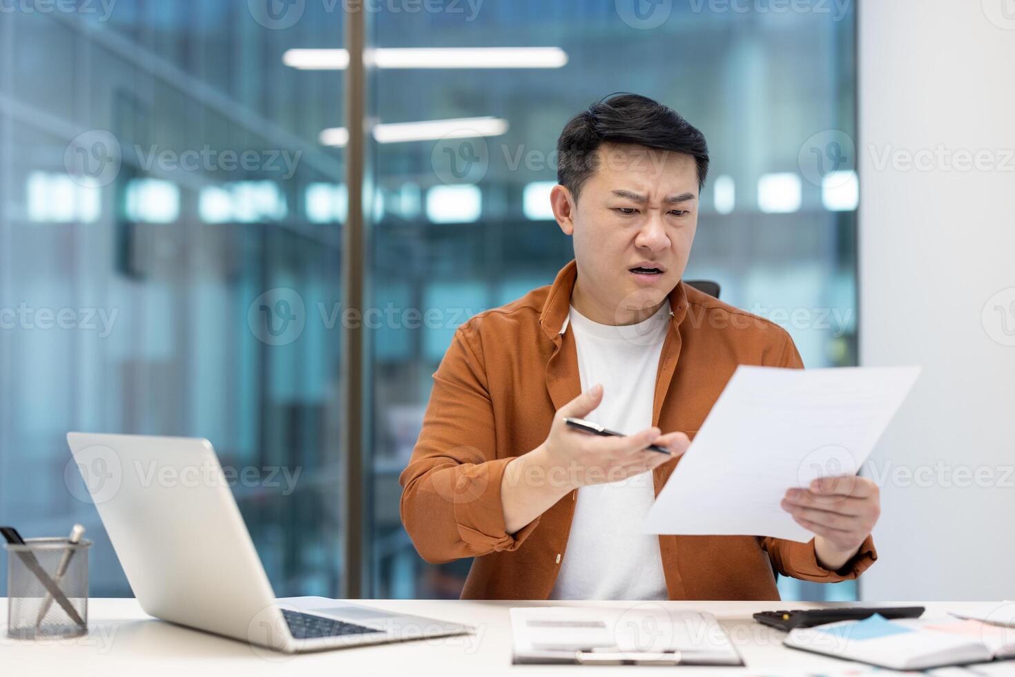 A concerned Asian businessman studies documents at his desk, possibly facing financial difficulties. photo