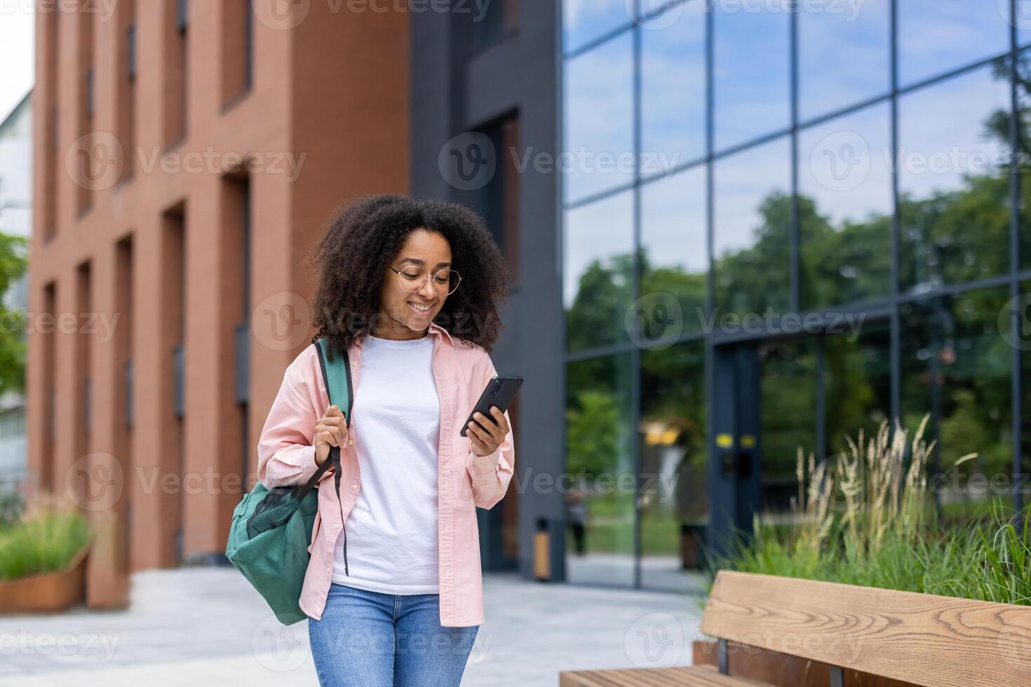 An African American student smiles while looking at her phone as she walks near a modern building. photo