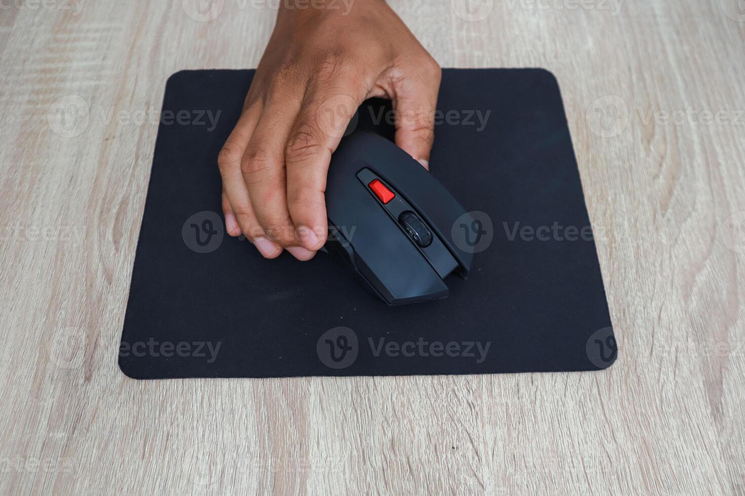 Hand Using A Black Wireless Mouse On A Wooden Desk photo
