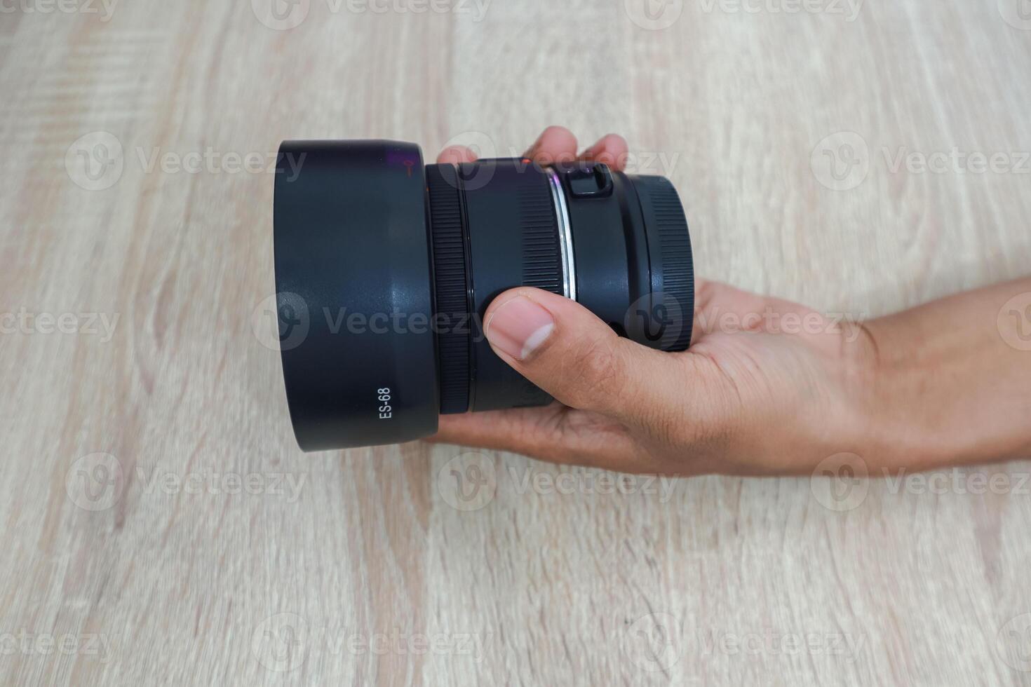 Hand Holding Camera Lens On Wooden Surface photo
