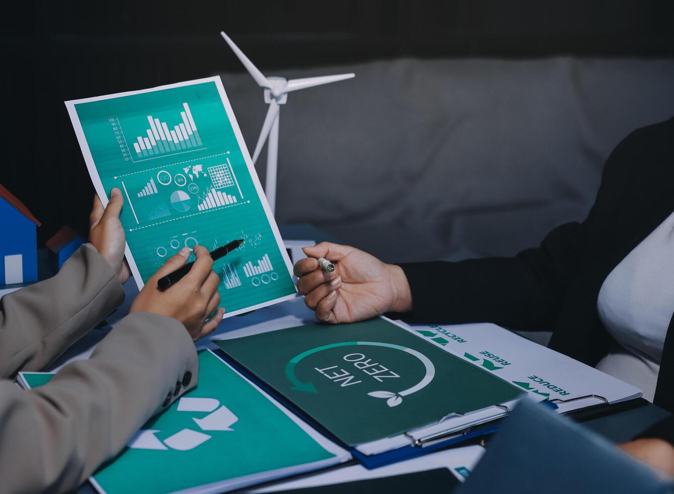 Two business people sitting at a table with papers and a wind turbine photo