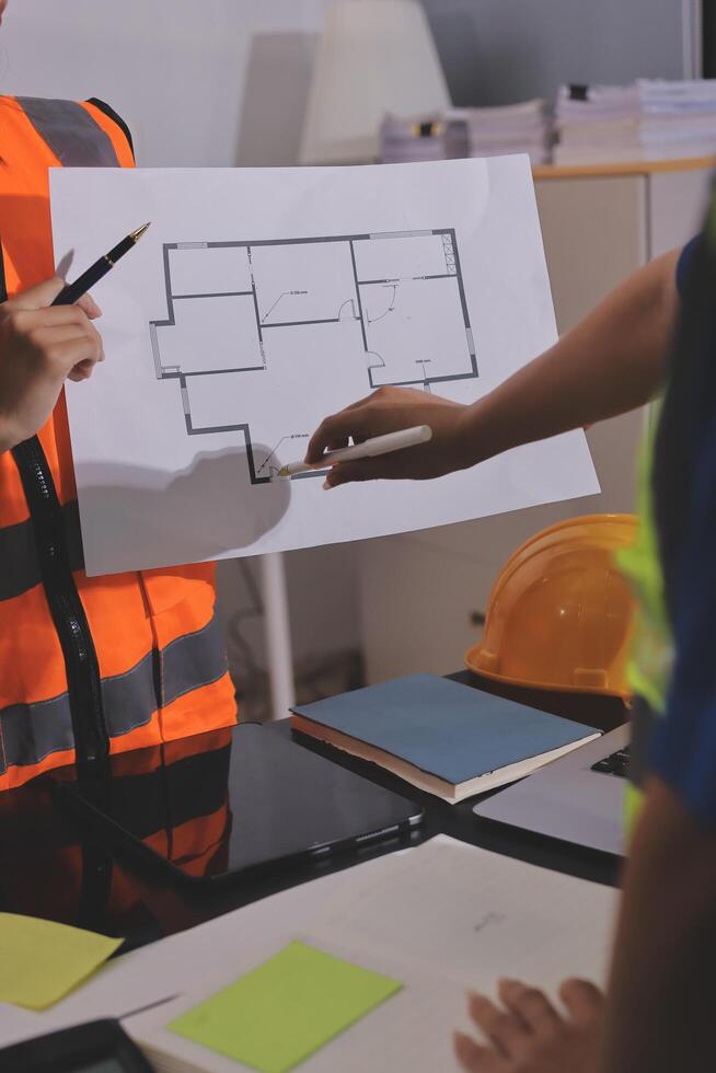 A man in an orange vest and safety vest is holding a blueprint photo
