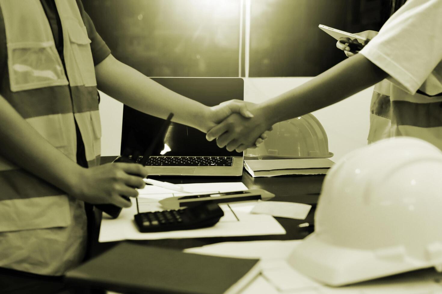 Two construction workers shaking hands over a desk photo