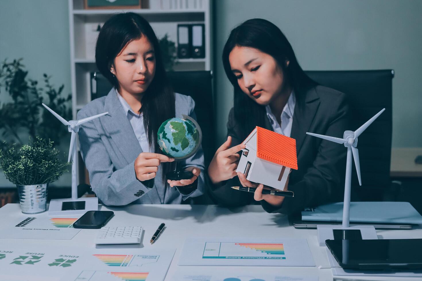 Two women in business attire holding a globe and wind turbines photo