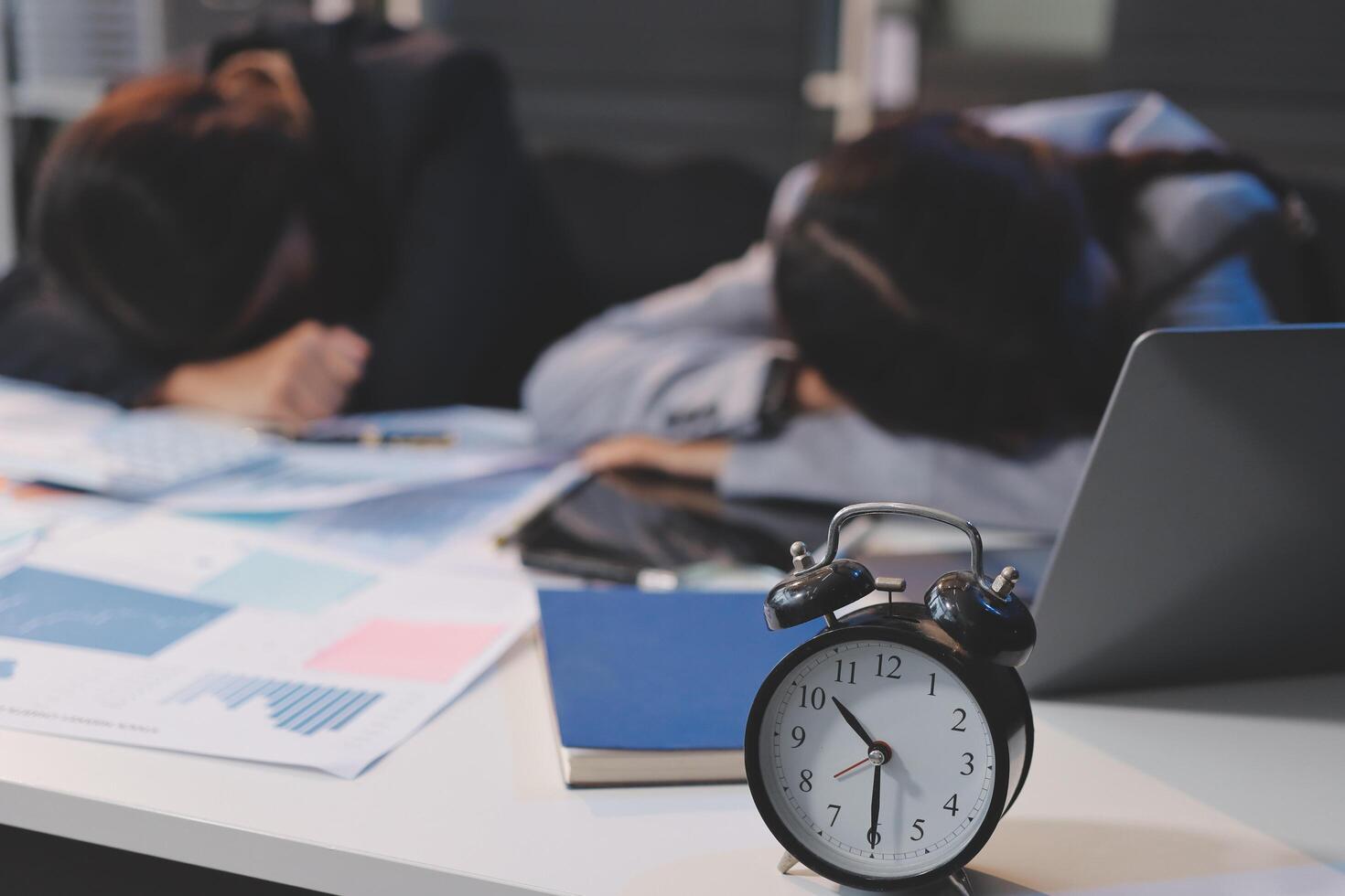 A woman sleeping on a desk with an alarm clock photo