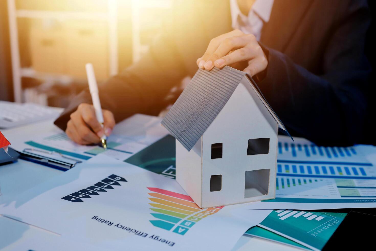 Businessman holding house model and financial report on table photo