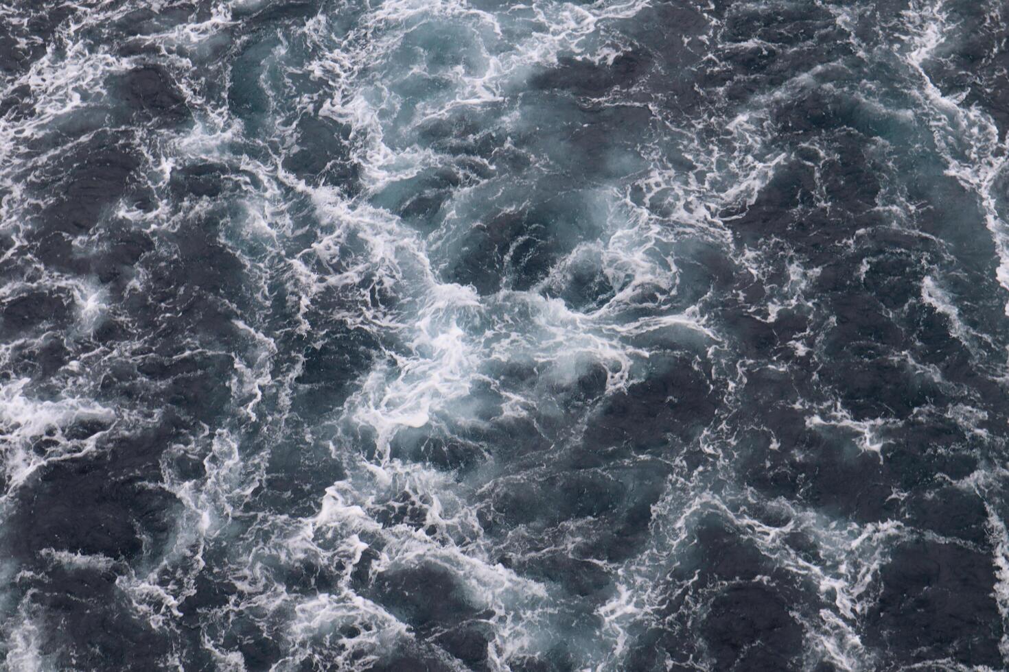 An aerial view of the ocean with white and black waves photo