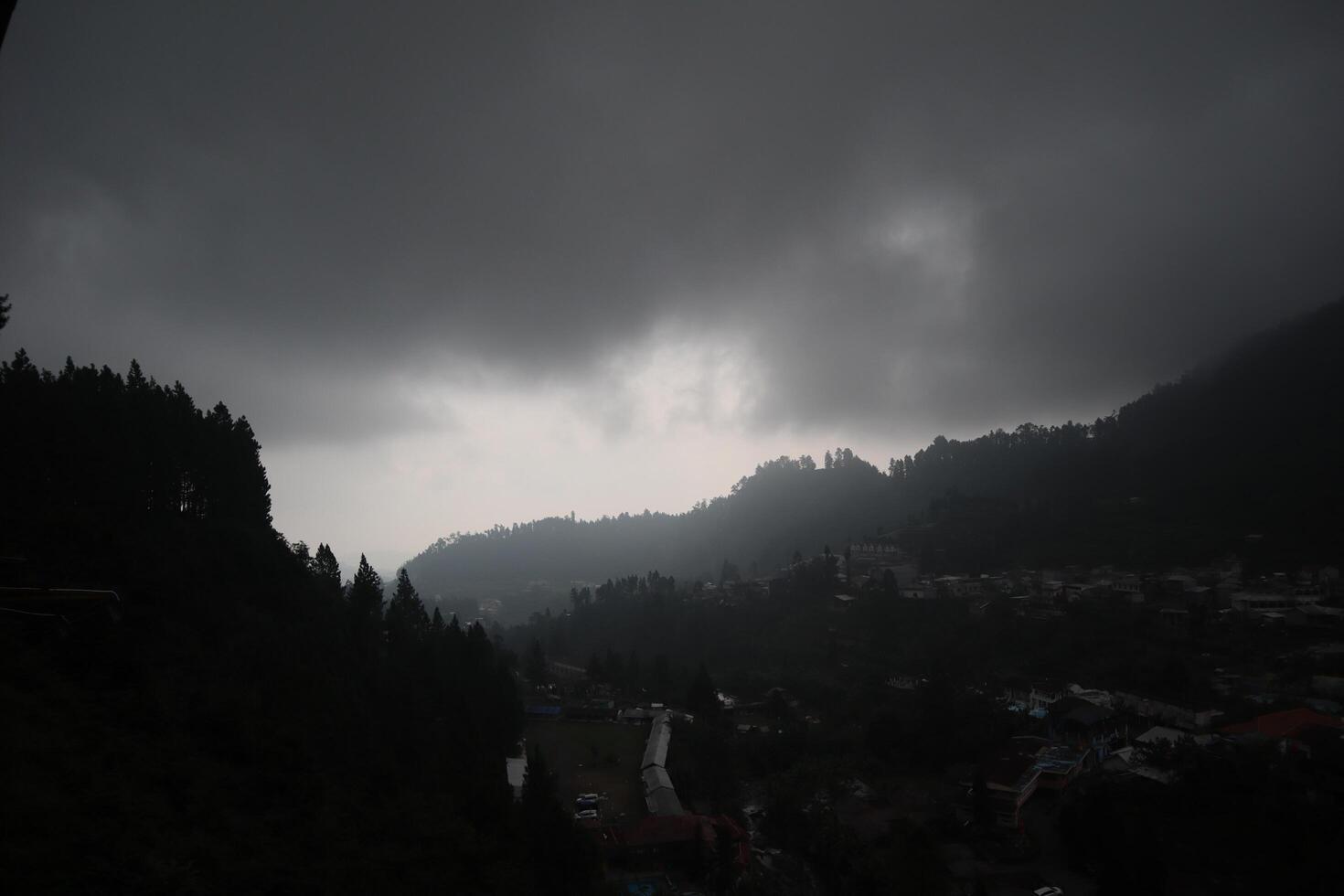 A dark sky over a town with trees and mountains photo