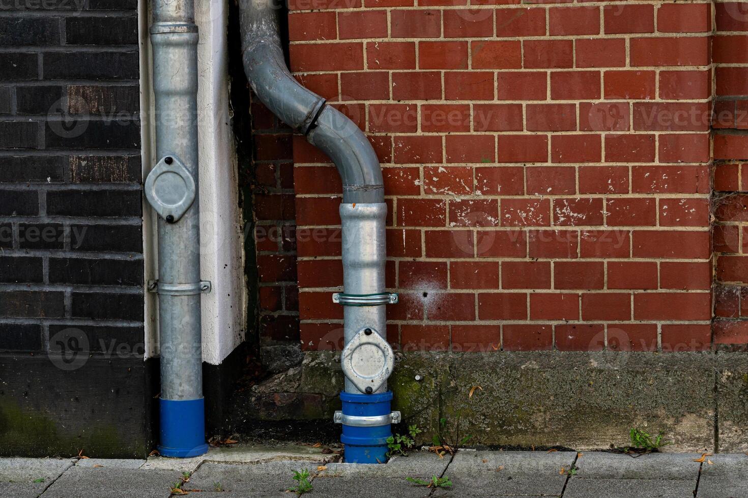 A metallic water pipe system is installed next to a red brick wall photo