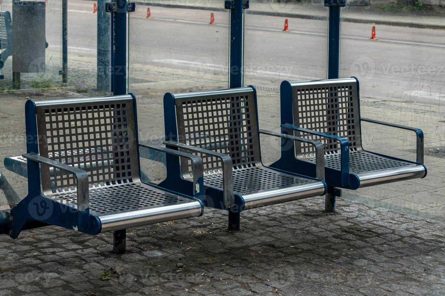 Three modern metal benches are positioned at a bus stop in an urban photo