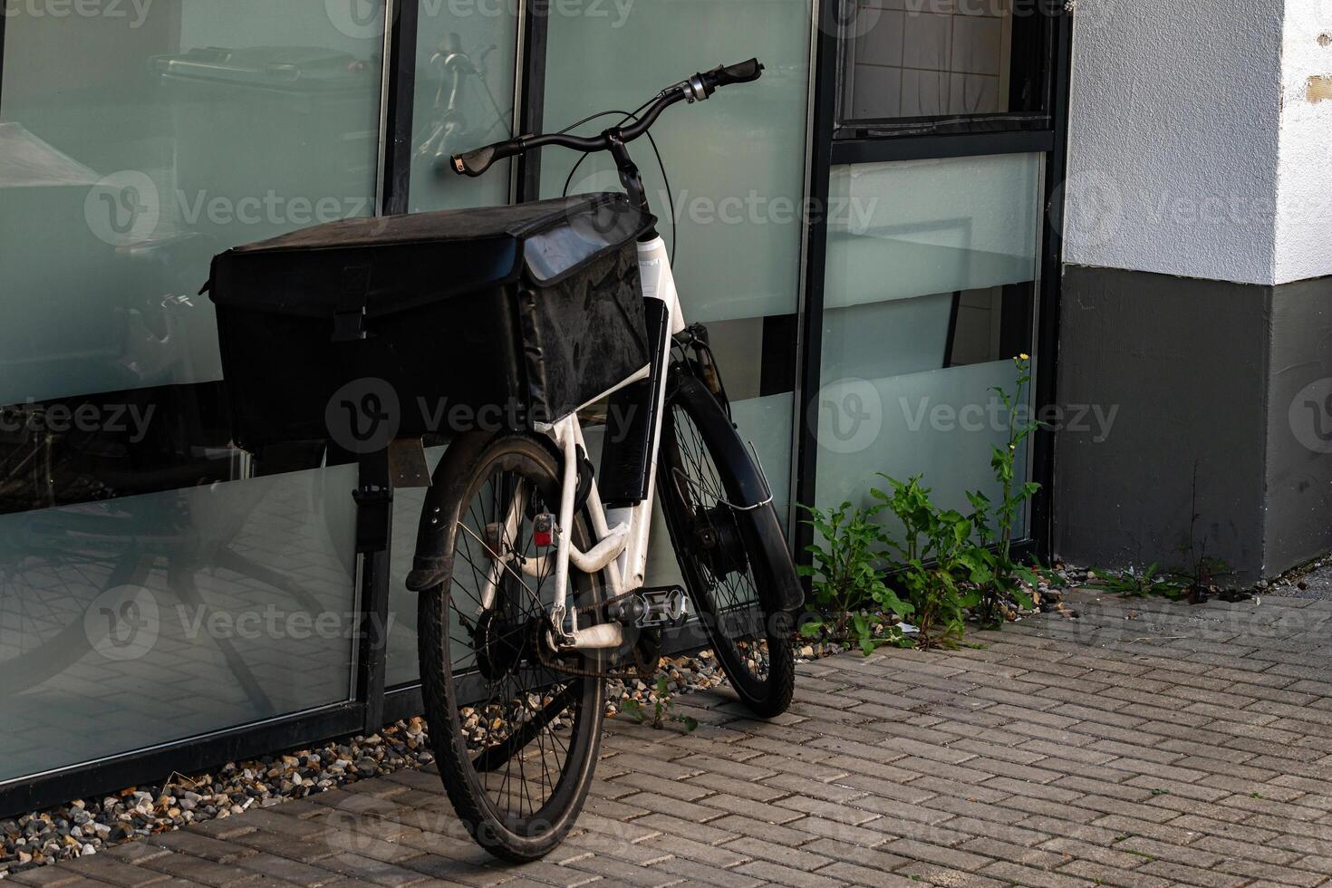 A delivery bicycle stands parked against a contemporary building. The photo