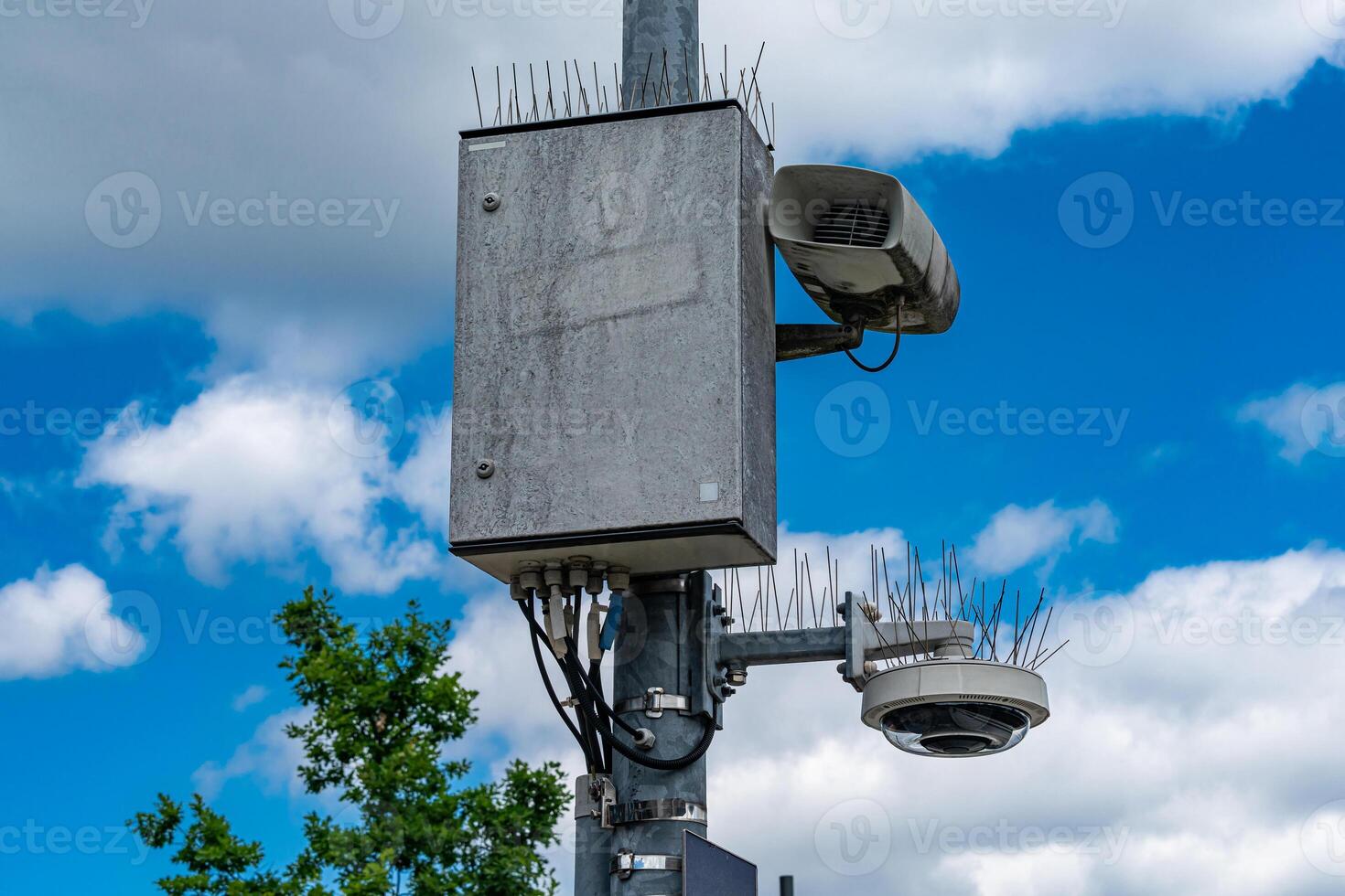 A concrete surveillance box sits on a tall pole alongside a camera and photo