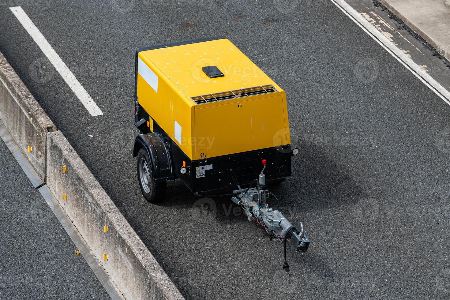 A yellow small trailer is parked on the shoulder of a highway. It is photo