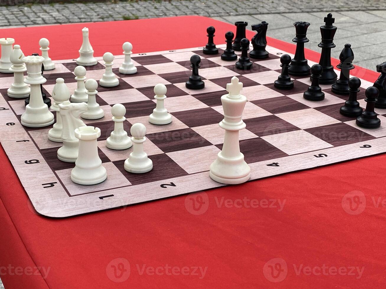 Outdoor chessboard setup with white and black chess pieces on red table background photo