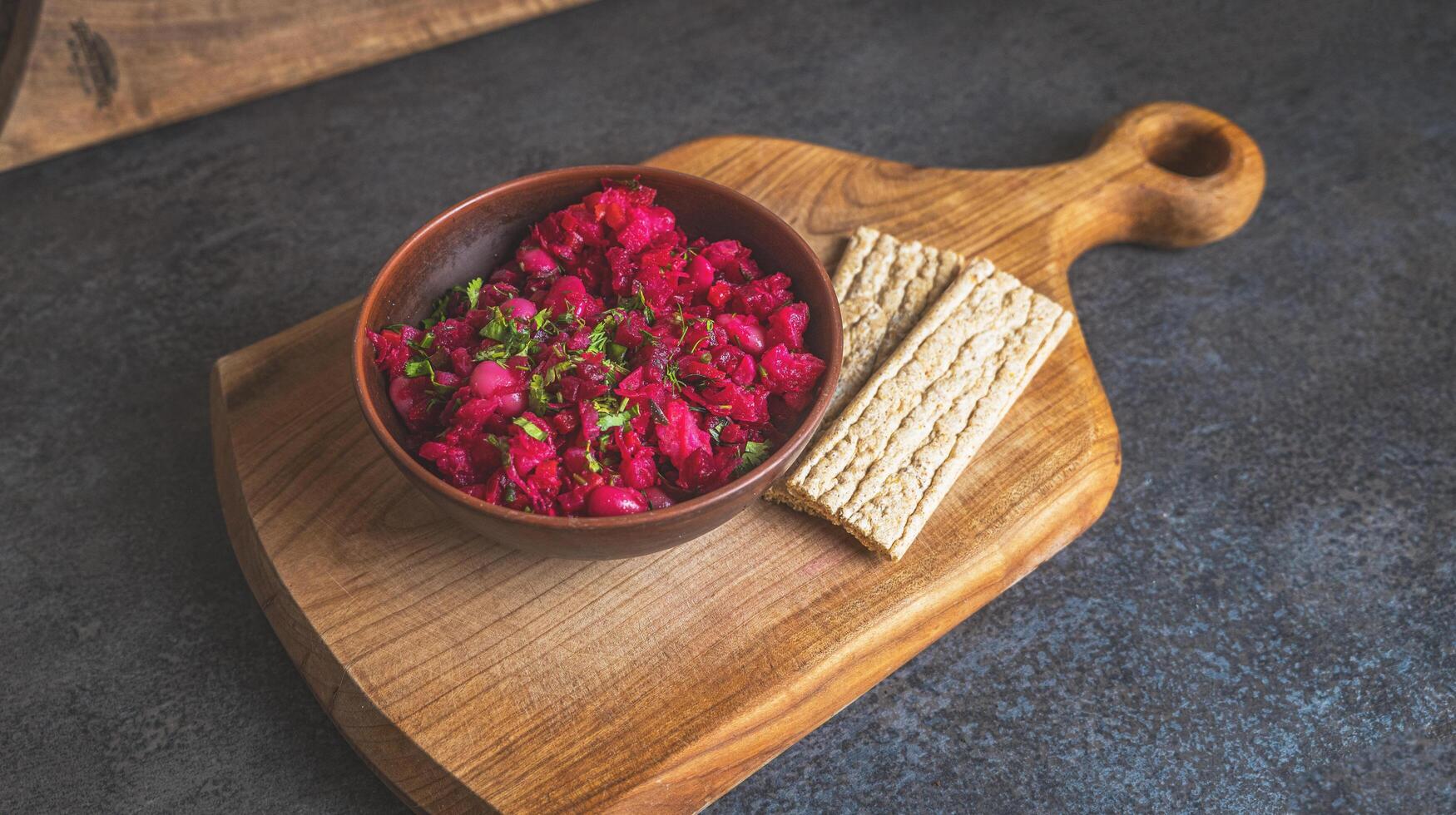 Healthy beetroot salad with herbs and beans served in a rustic bowl on a wooden cutting board with crispbread. Natural light and cozy kitchen atmosphere photo