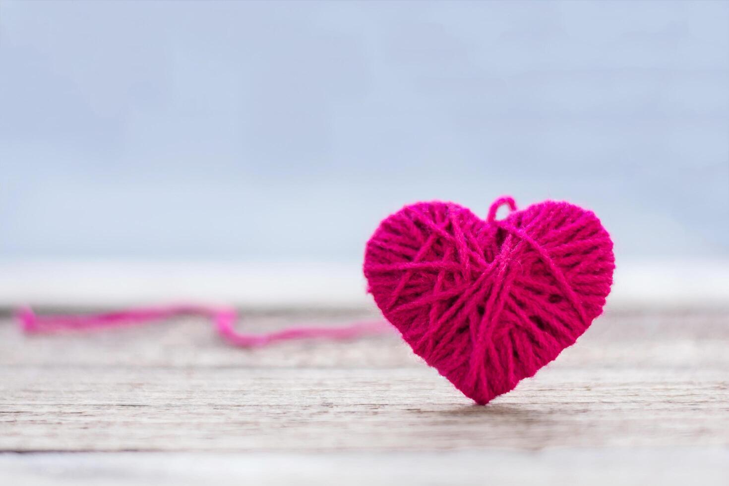red knitting wool in shape of heart on vintage wooden with bokeh soft light background. photo