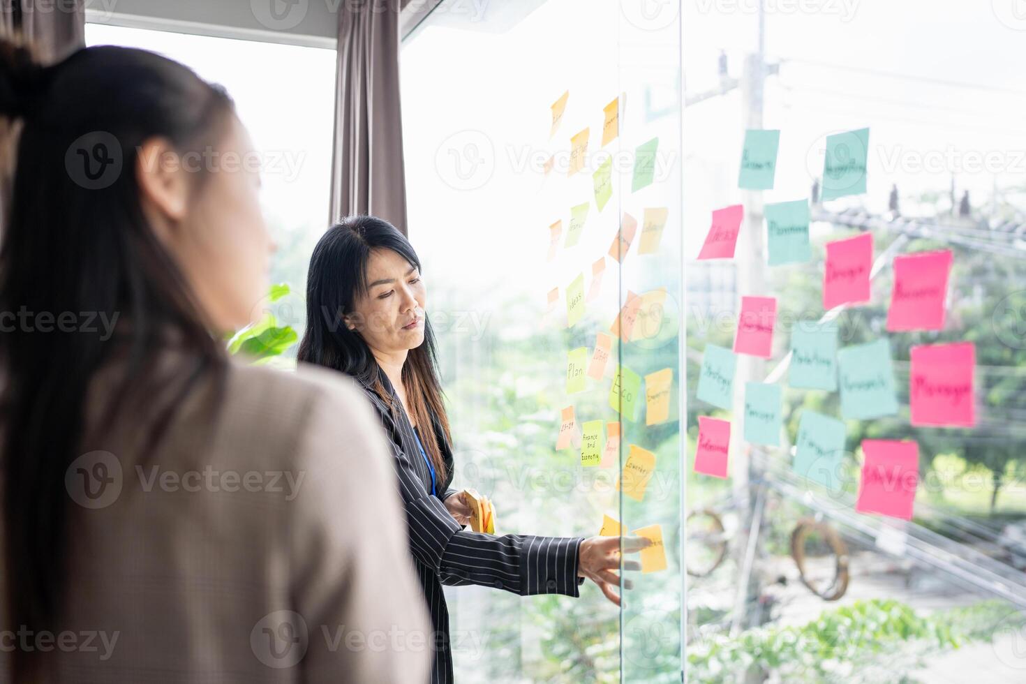 two women looking at sticky notes on a glass window photo