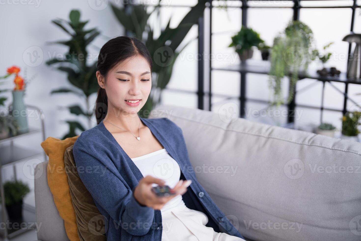 asian woman sitting on couch holding remote control photo