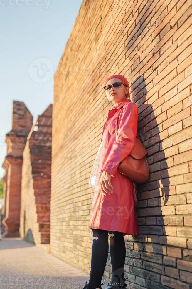 Traveler girl woman in a red coat and sunglasses leaning against a brick wall photo