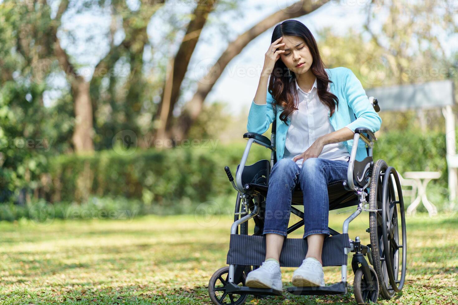 Depressed sad woman in a wheelchair sitting on the grass. photo