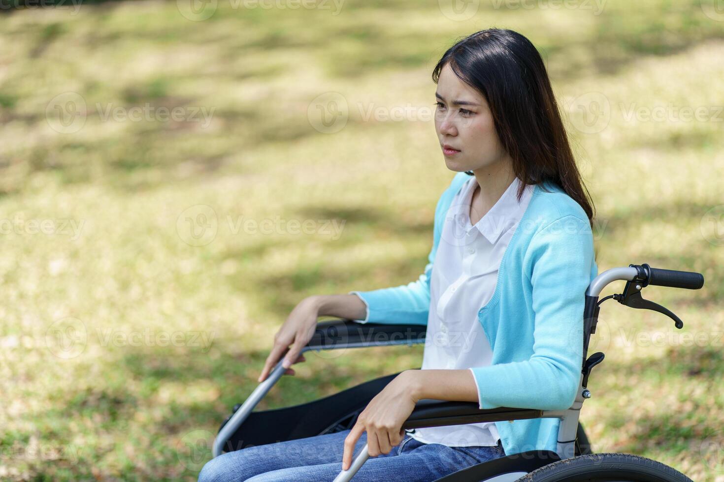 Depressed sad woman in a wheelchair sitting on the grass photo